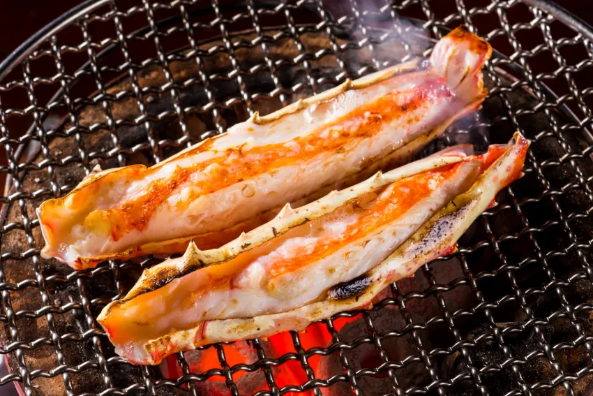 三燔本家「頂級鱈場蟹饗宴」中的炭烤鱈場蟹腳是選用鱈場蟹腳後段，肉質厚實飽滿，以熱度均勻的炭火慢烤而成，香氣迷人。圖/台北晶華提供